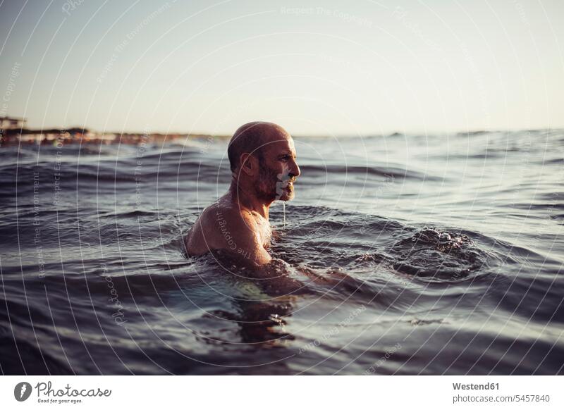 Senior man swimming in sea during sunset color image colour image outdoors location shots outdoor shot outdoor shots sunsets sundown atmosphere Idyllic