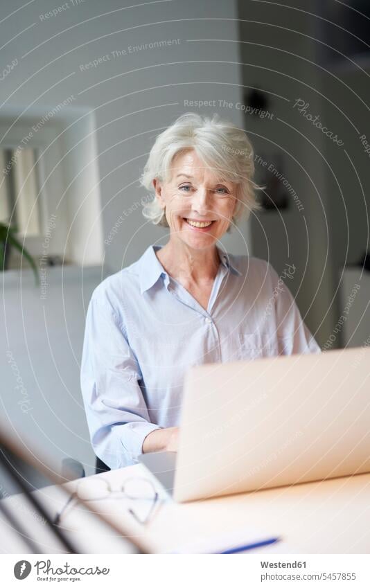 Portrait of smiling mature woman using laptop at desk Occupation Work job jobs profession professional occupation business attire business clothing Tables desks