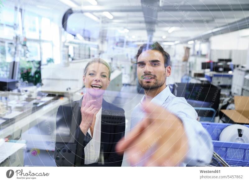 Cheerful mature businesswoman standing by businessman pointing at glass interface at factory color image colour image indoors indoor shot indoor shots interior