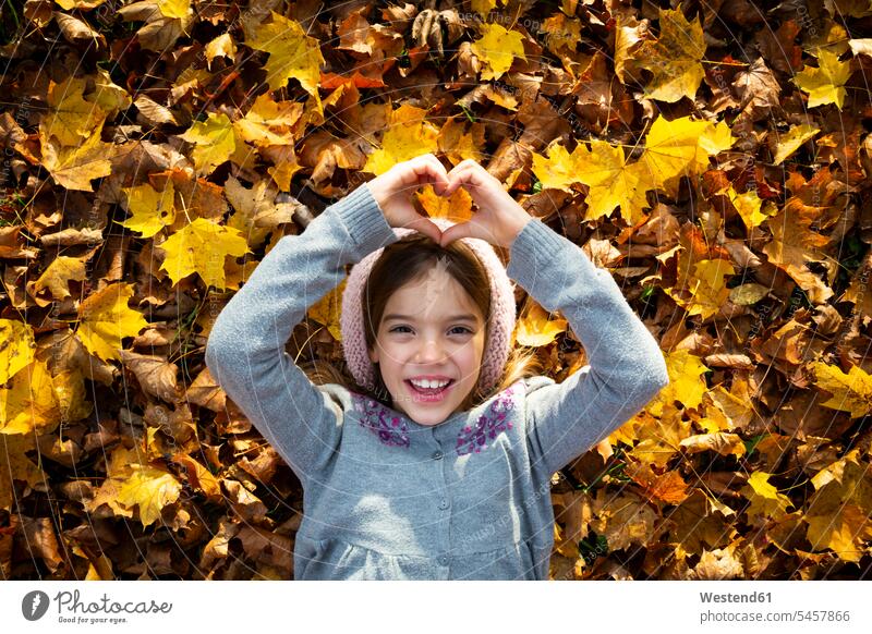 Portrait of happy little girl lying on autumn leaves shaping heart with her hands portrait portraits Forming hearts heart shapes autumn foliage human hand