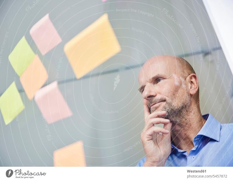 Thoughtful businessman reading adhesive note while standing by glass wall color image colour image indoors indoor shot indoor shots interior interior view