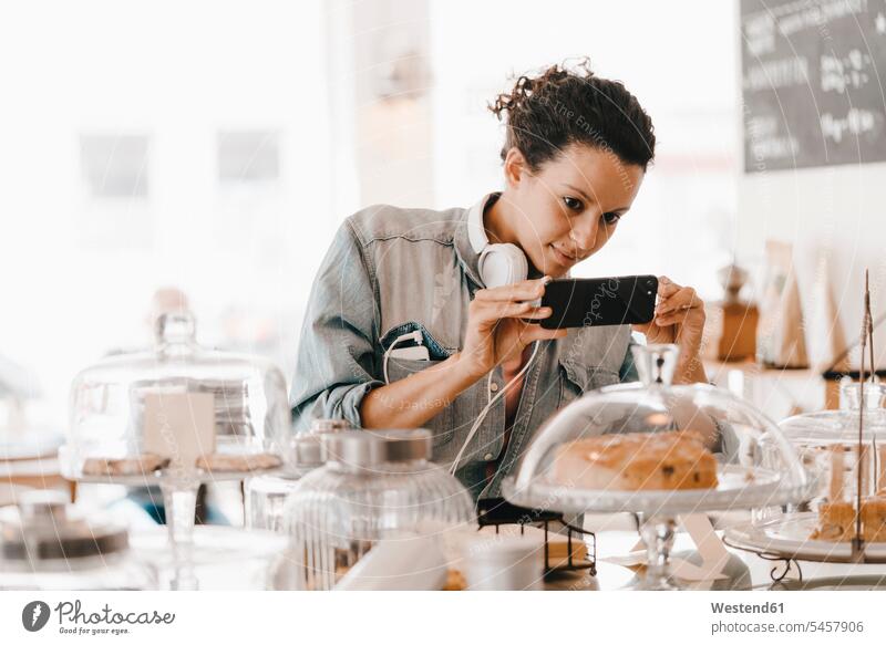 Woman taking pictures of cakes in coffee shop with her smartphone cafe headphones headset pies Smartphone iPhone Smartphones woman females women Sweet Food