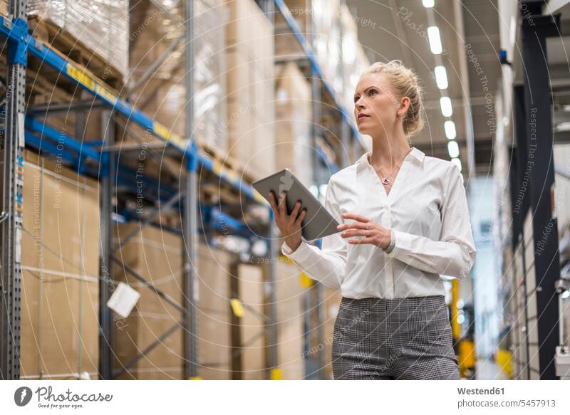 Woman with tablet in factory storehouse looking at shelf industrial hall shop floor factory hall industrial buildings woman females women eyeing factories
