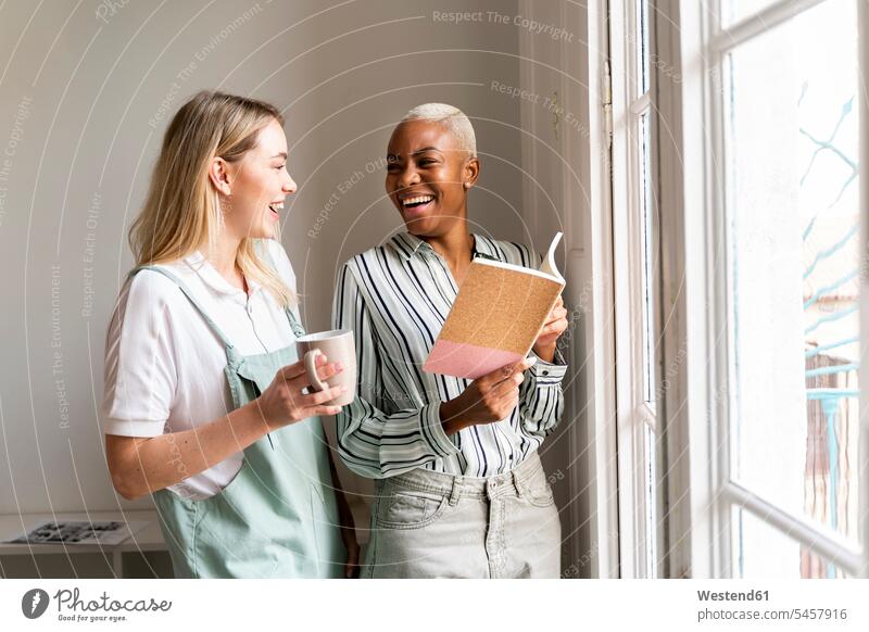 Two happy women with notebook and cup of coffee at the window Occupation Work job jobs profession professional occupation business life business world