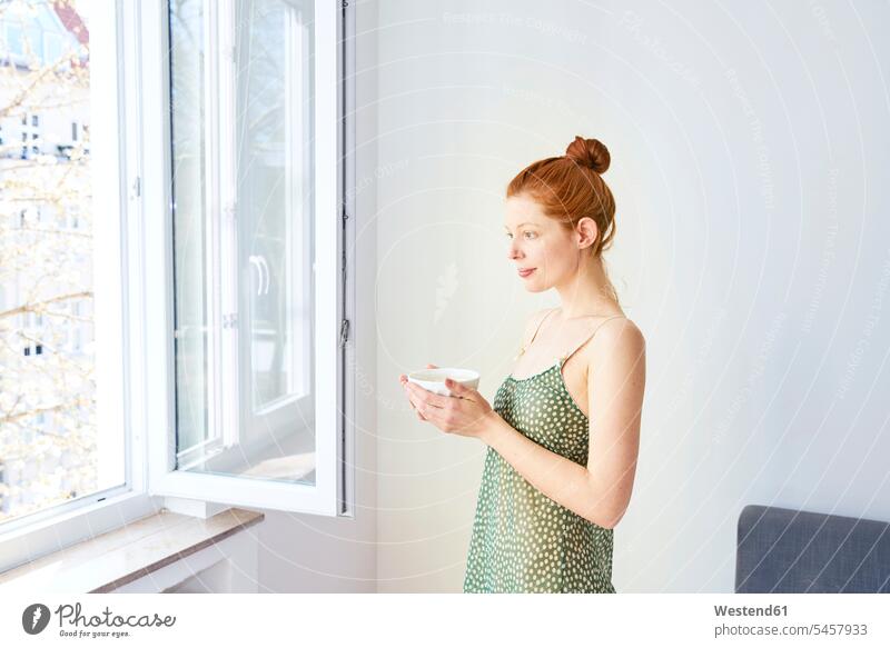 Portrait of pensive woman with bowl of white coffee standing near open window females women Coffee Bowl Bowls windows thoughtful Reflective contemplative