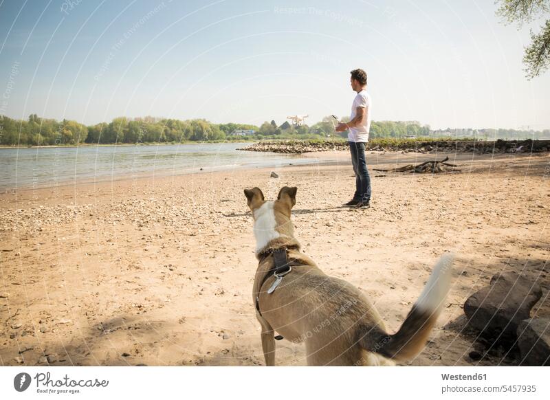 Man with a dog flying drone at a river River Rivers dogs Canine drones man men males water waters body of water pets animal creatures animals Adults grown-ups
