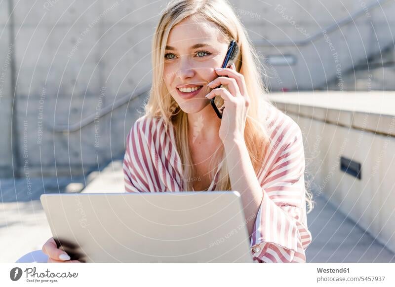 Portrait of smiling blond young woman with laptop on the phone outdoors females women Laptop Computers laptops notebook smile call telephoning On The Telephone