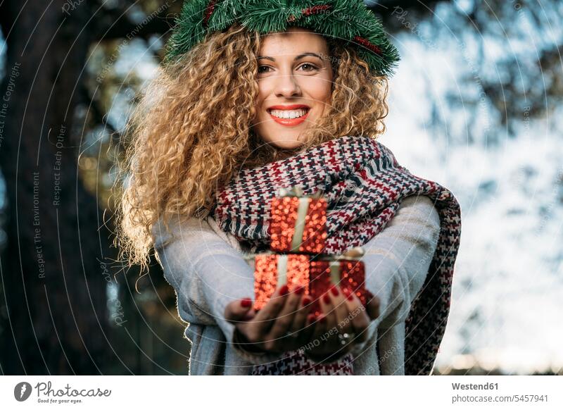 Portrait of smiling young woman with Christmas wreath on her head presenting Christmas present scarfs scarves give smile in the evening delight enjoyment