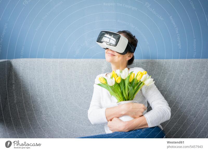 Smiling woman sitting on couch wearing VR glasses holding bunch of tulips females women Bunch of Flowers Bouquet Flower Bouquet Bouquet of Flowers