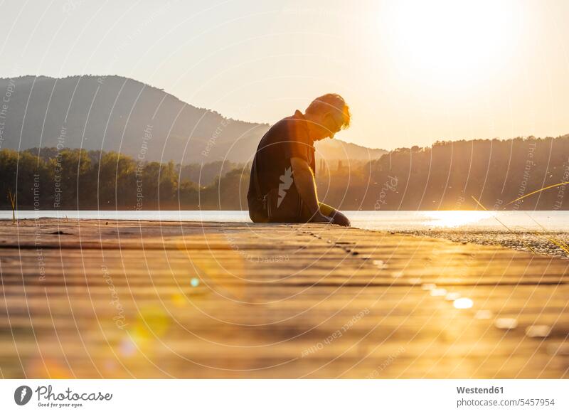 Senior man sitting on a wooden footbridge and looking down, against the sun human human being human beings humans person persons caucasian appearance