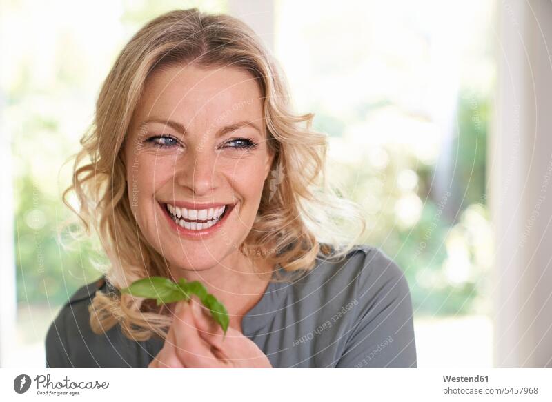 Portrait of smiling woman holding basil in kitchen Basil leaf Basil Leaves Basils smile portrait portraits domestic kitchen kitchens females women culinary herb
