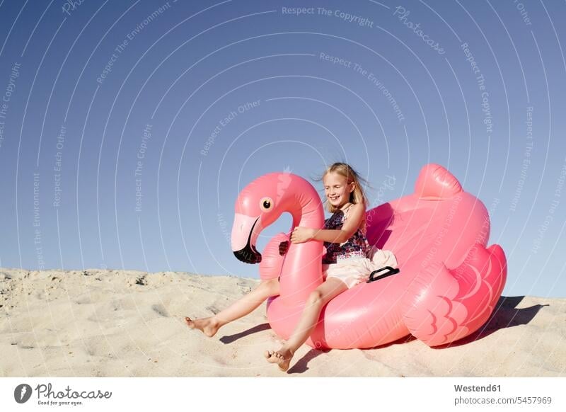 Smiling little girl with flamingo pool float on the sand air bed air beds air mattress air mattresses airbeds inflatable mattress lilo lilos toys Seated sit