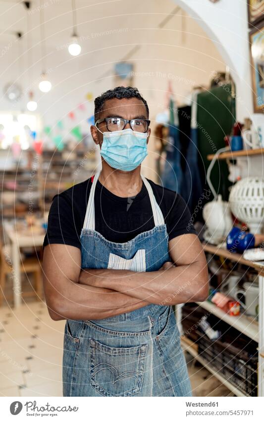 Male potter wearing mask with arms crossed standing in workshop color image colour image Spain indoors indoor shot indoor shots interior interior view Interiors