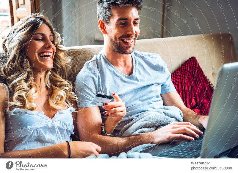 Happy young couple sitting on couch at home with credit card and laptop finance financial credit cards debit card direct payment couches settee settees sofa