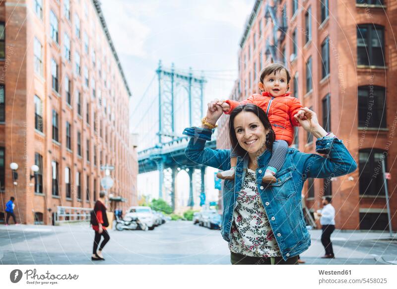 USA, New York, New York City, Mother and baby in Brooklyn with Manhattan Bridge in the background on shoulders daughter daughters childhood smiling smile