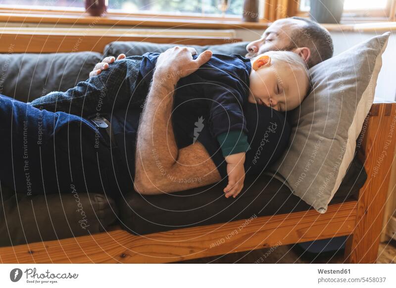 Father and son sleeping together on the sofa cushions couches settee settees sofas relax relaxing cuddle snuggle snuggling asleep embrace Embracement hug