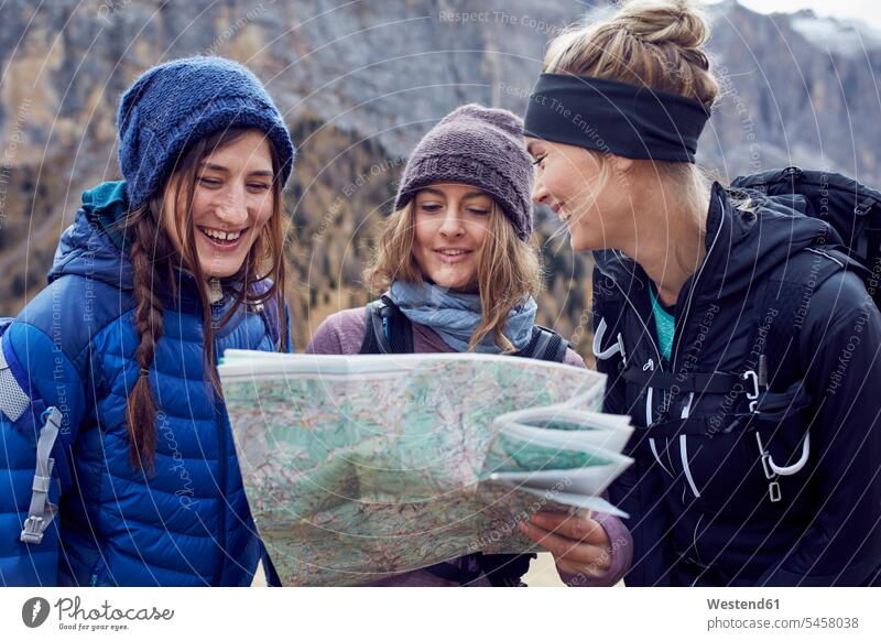 Three happy young women hiking in the mountains looking at map maps hike female friends eyeing happiness woman females mate friendship view seeing viewing