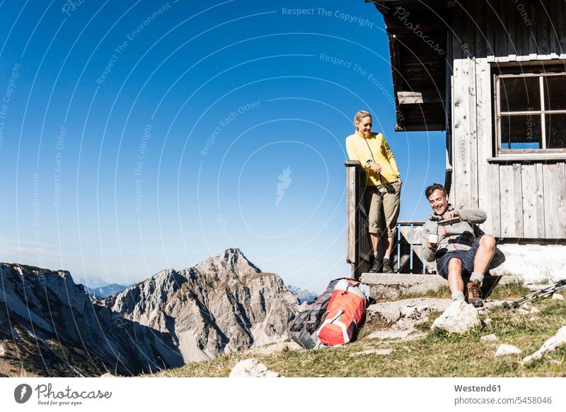 Hiking couple sitting in front of mountain hut, taking a break mountain pasture mountain shelter alpine hut mountain huts mountain lodge mountain range