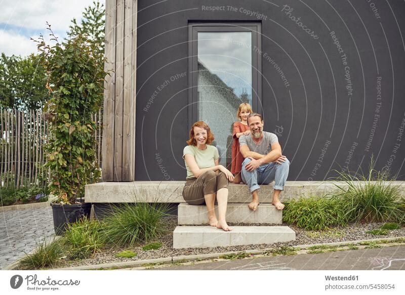 Smiling parents with girl sitting on steps outside tiny house color image colour image Germany leisure activity leisure activities free time leisure time