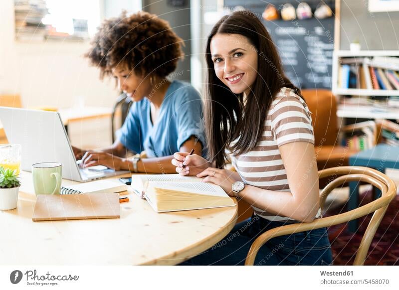 Happy female friends studying with laptop at table in coffee shop color image colour image indoors indoor shot indoor shots interior interior view Interiors day