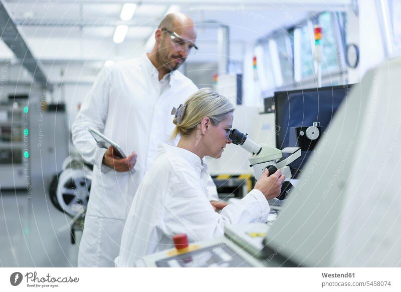 Male technician standing by female scientist looking into microscope while doing research in laboratory color image colour image indoors indoor shot