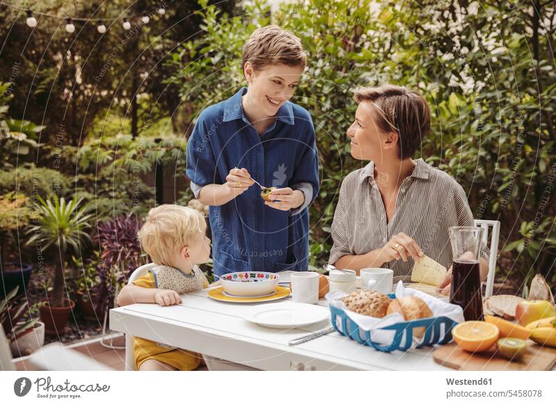 Two happy mothers at breakfast table outdoors with their child happiness Breakfast children Breakfast Table Breakfast Tables mommy ma mummy mama Meals Food