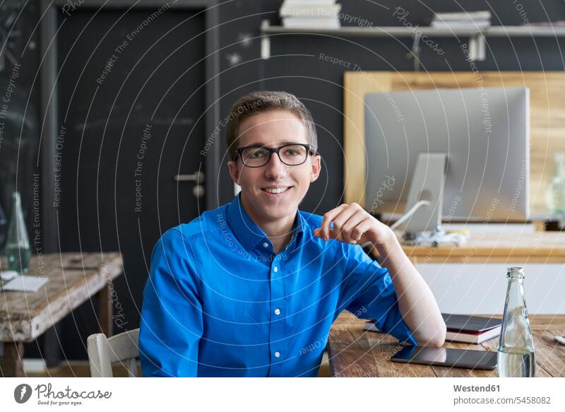 Portrait of smiling young man at wooden table in office smile portrait portraits offices office room office rooms men males Table Tables workplace work place