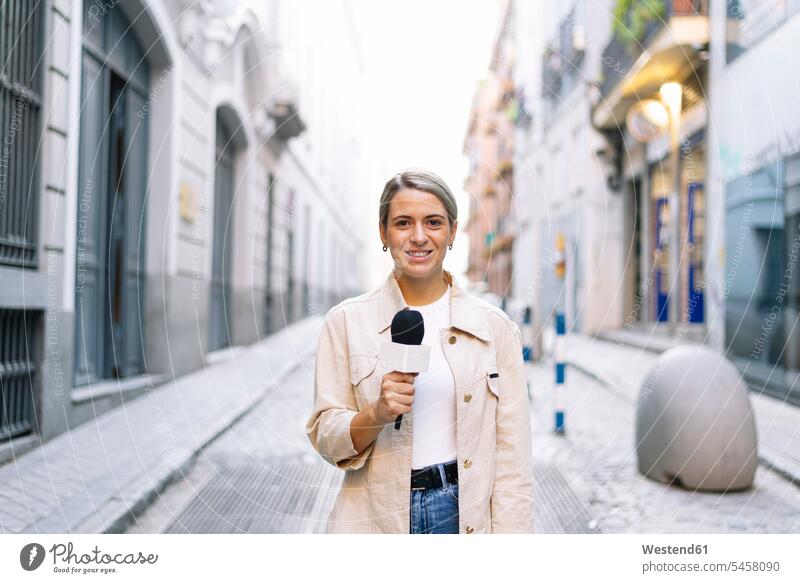 Female journalist talking over microphone while standing on street in city color image colour image Spain outdoors location shots outdoor shot outdoor shots day