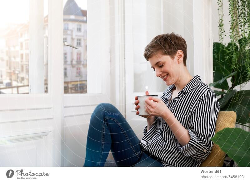 Happy woman sitting relaxed at window, drinking coffee relaxation happiness happy Seated windows Coffee females women relaxing Drink beverages Drinks Beverage