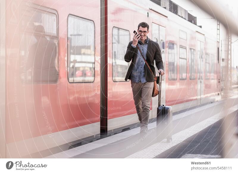 Happy young man with cell phone walking on station platform along commuter train going Railroad Platform train station happiness happy men males mobile phone