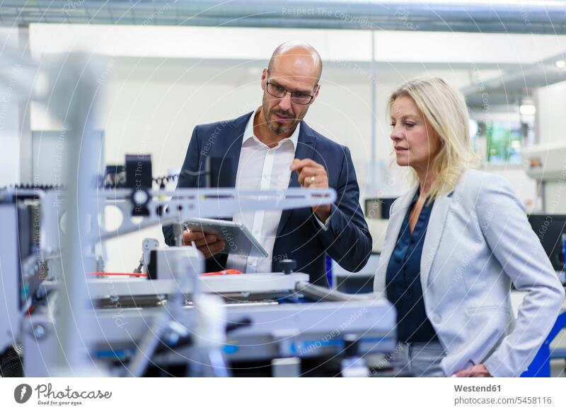 Confident businessman and businesswoman discussing while looking at machinery in factory color image colour image indoors indoor shot indoor shots interior