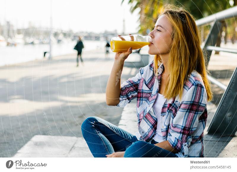 Young woman drinking juice while sitting on footpath in city color image colour image outdoors location shots outdoor shot outdoor shots day daylight shot