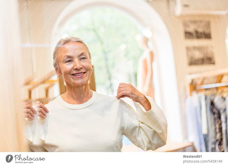 Smiling senior woman trying on pullover in a boutique sweater jumper Sweaters senior women elder women elder woman old shopping females boutiques fit fitting