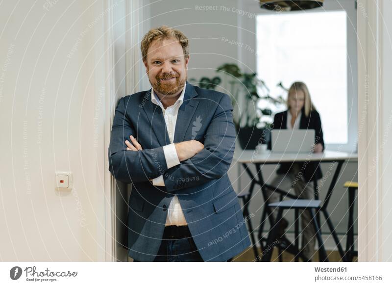Portrait of confident businessman in office with businesswoman in background human human being human beings humans person persons caucasian appearance