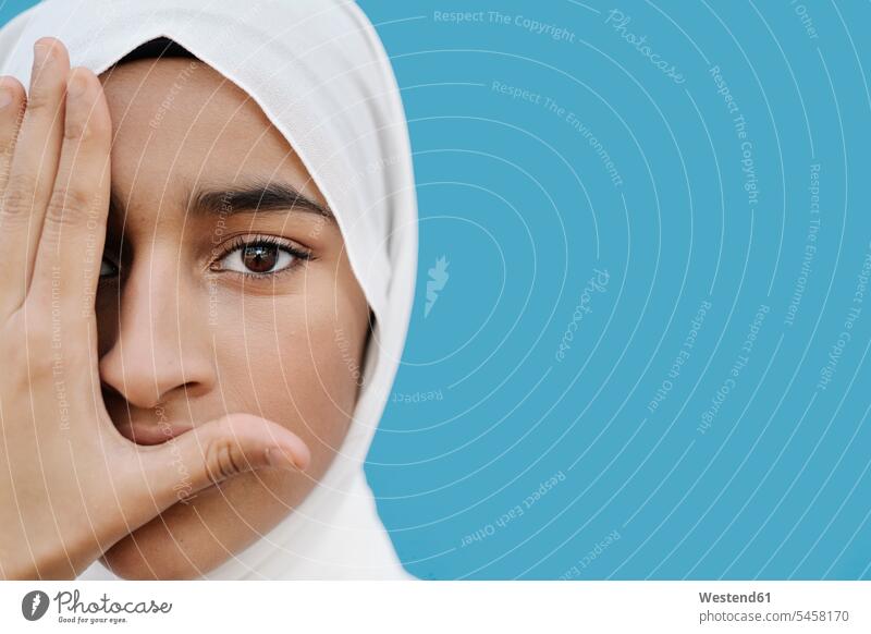 Muslim girl covering eye with hand against blue background color image colour image studio shot studio photograph studio photographs studio shots indoors