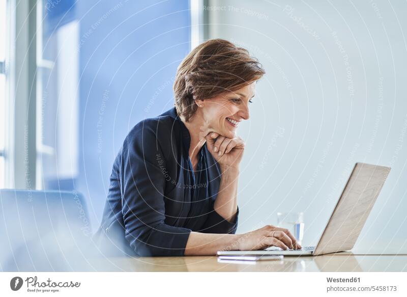 Smiling businesswoman using laptop at desk in office Occupation Work job jobs profession professional occupation business life business world business person