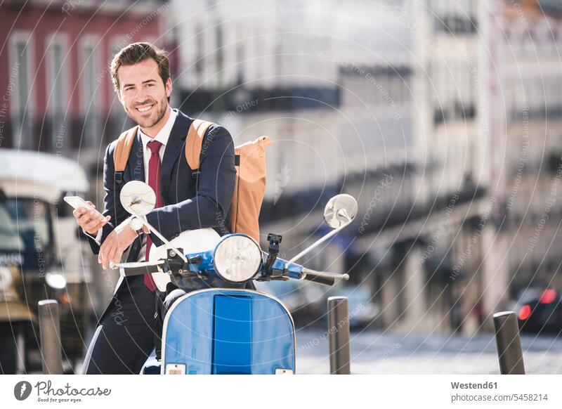 Smiling young businessman with cell phone and motor scooter in the city, Lisbon, Portugal business life business world business person businesspeople