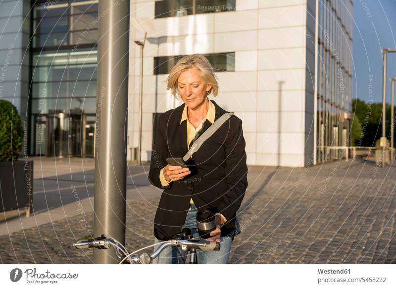 Senior woman with city bike and takeaway coffee using cell phone Coffee females women bicycle bikes bicycles mobile phone mobiles mobile phones Cellphone
