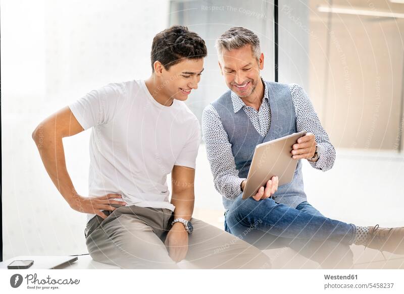 Senior businessman working with young colleague, using digital tablet human human being human beings humans person persons caucasian appearance