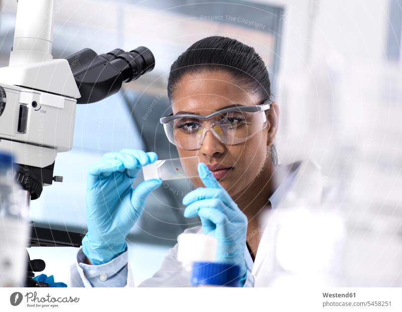 Female scientist examining a human sample on a microscope slide specimen trials specimens working At Work blood human blood woman females women science sciences