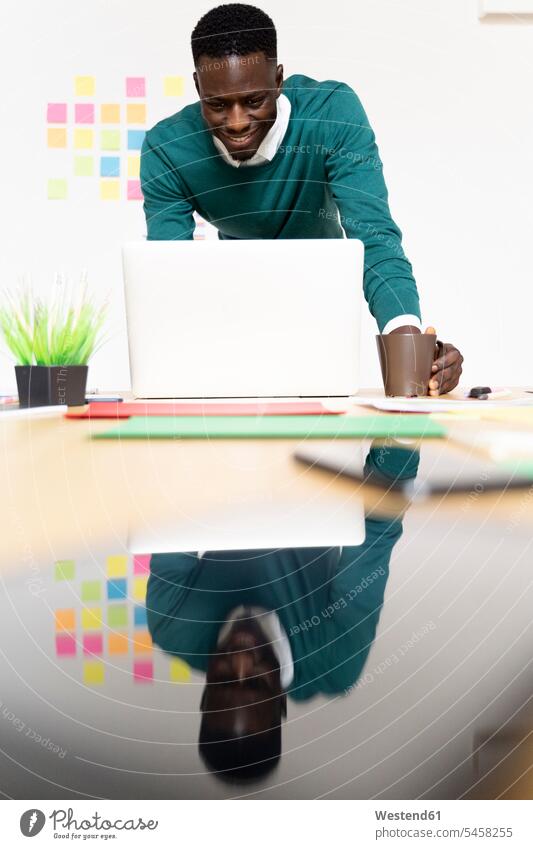 Smiling man working on laptop at desk in office human human being human beings humans person persons African black black ethnicity coloured 1 one person only