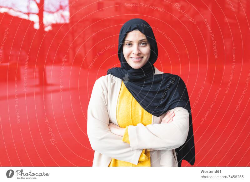 Portrait of smiling young woman wearing hijab in front of red glass pane human human being human beings humans person persons Middle Eastern 1 one person only