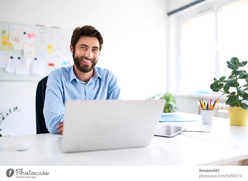 Portrait of a smiling businessman sitting at a desk using a laptop Occupation Work job jobs profession professional occupation Design Occupation