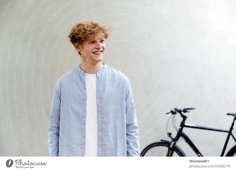 Portrait of smiling young man with curly blond hair standing in front of grey wall human human being human beings humans person persons caucasian appearance