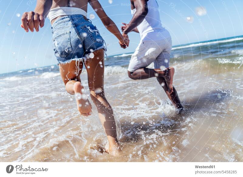 Playful couple holding hands while running in sea against clear sky color image colour image Spain leisure activity leisure activities free time leisure time