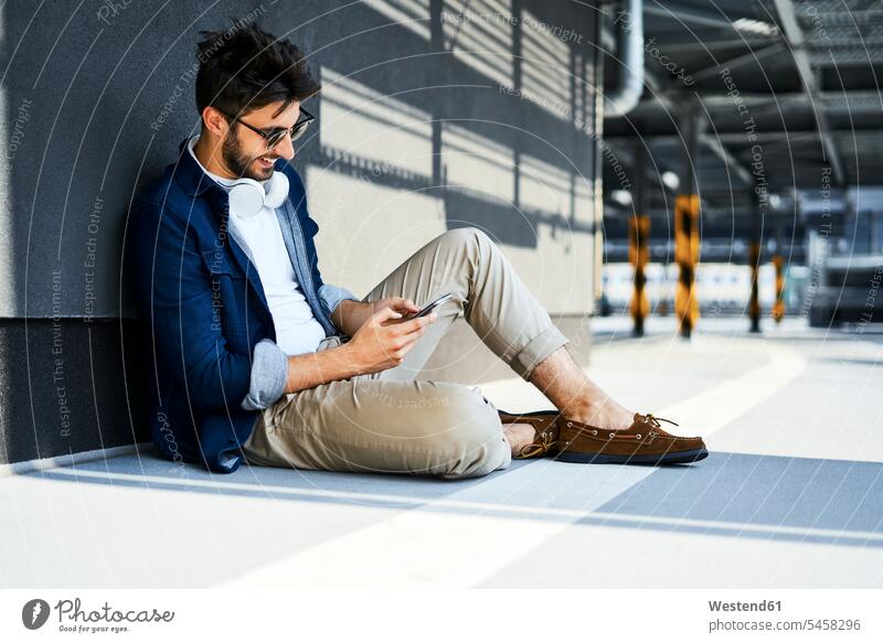 Smiling young man sitting on the ground using smartphone smiling smile use Smartphone iPhone Smartphones land floor men males Seated mobile phone mobiles