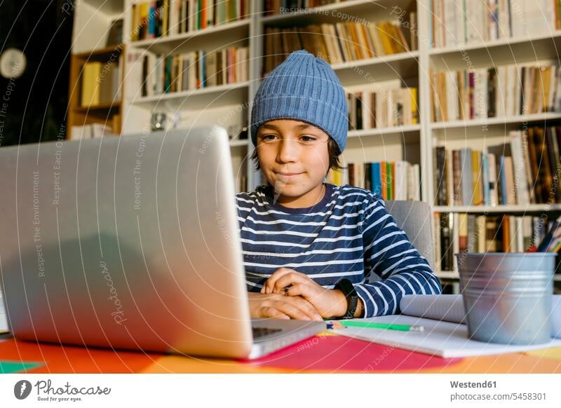 Boy attending homeschooling class through laptop at table in living room color image colour image 10-11 years 10 to 11 years children kid kids people