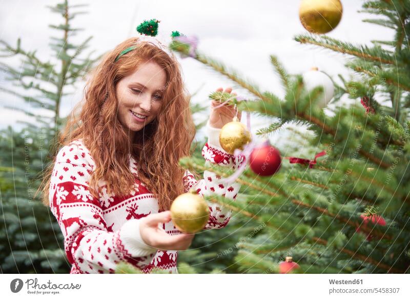 Portrait of redheaded young woman decorating Christmas tree outdoors portrait portraits decorate females women Christmas trees decorated red hair red hairs