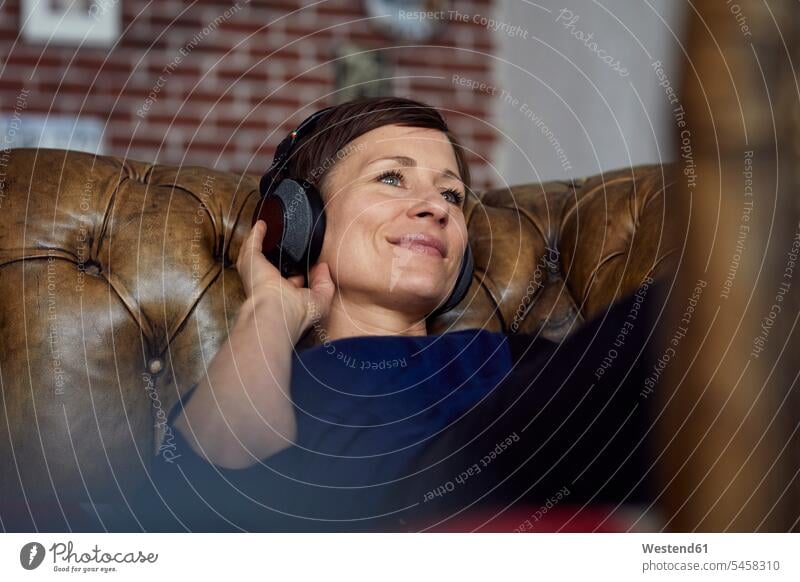 Woman with headphone lying on sofa, listening music laying down lie lying down couch settee sofas couches settees headphones headset woman females women hearing