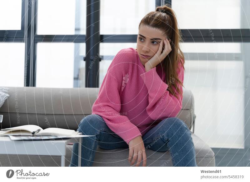 Portrait of pensive young woman sitting on the couch couches settee settees sofa sofas Seated contemplative pensively Reflective thoughtful colour colours
